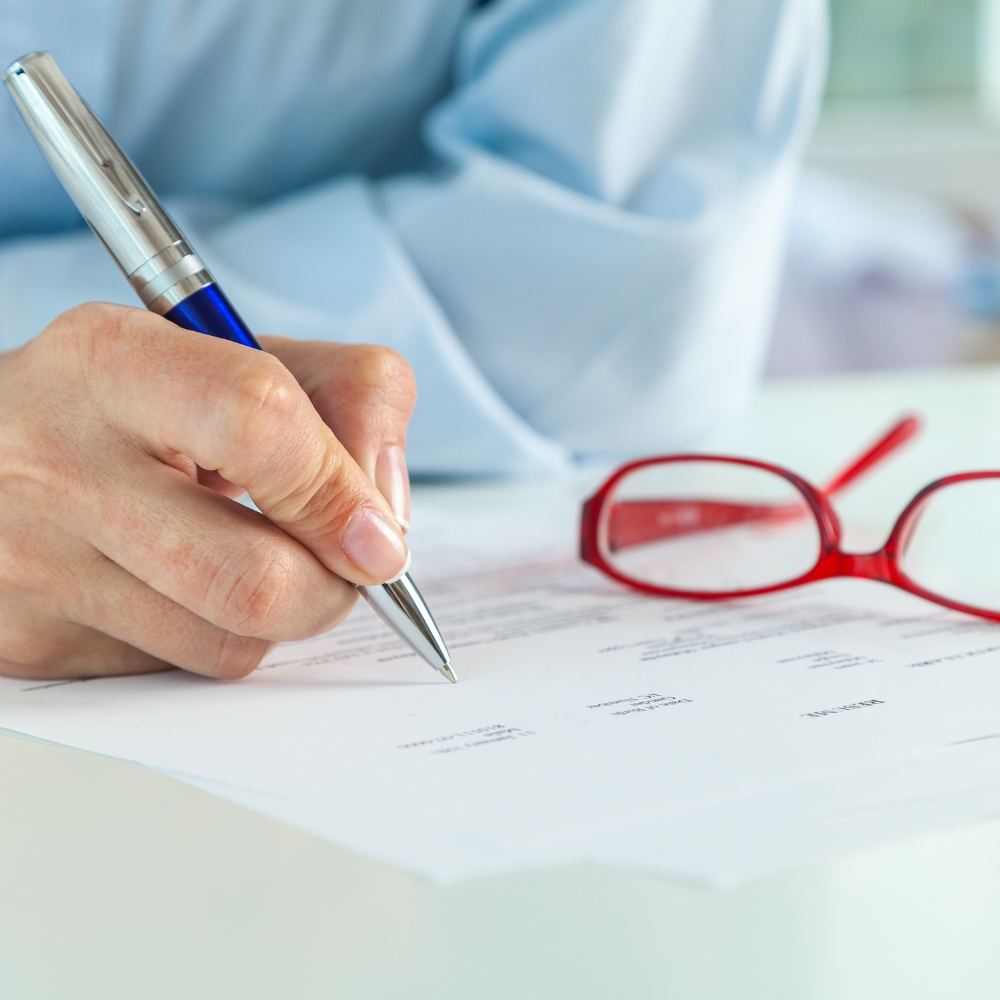 Close up of hand writing on paper on a desk with glasses